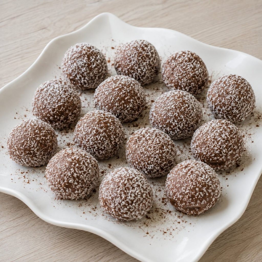 Handgemaakte kokostruffels met melkchocolade, gerold door kokosrasp, op een wit bord