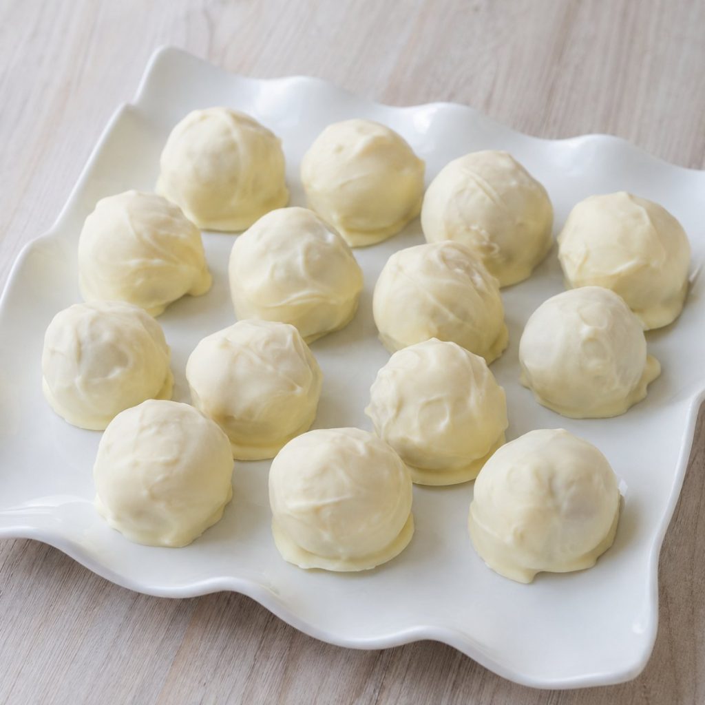 Handgemaakte slagroomtruffels omhuld met witte Callebaut-chocolade, op een wit bord